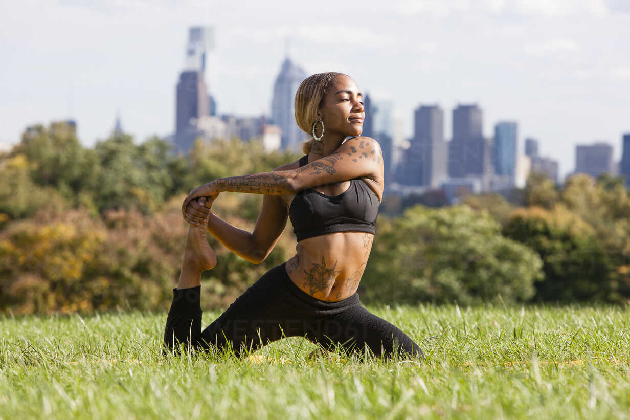 Front view of young woman kneeling on grass stretching leg in yoga
