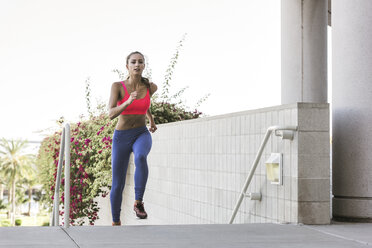 Young woman wearing sports clothing running up stairway looking at camera - ISF11365