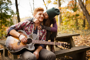 Romantisches junges Paar spielt Gitarre auf einer Picknickbank im Herbstwald - ISF11370