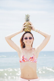 Porträt einer mittleren erwachsenen Frau am Strand, mit Sonnenbrille, Ananas auf dem Kopf haltend - ISF11396