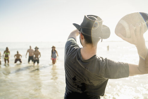 Junger Mann wirft American-Football-Ball zu Freunden ins Meer am Newport Beach, Kalifornien, USA - ISF11463