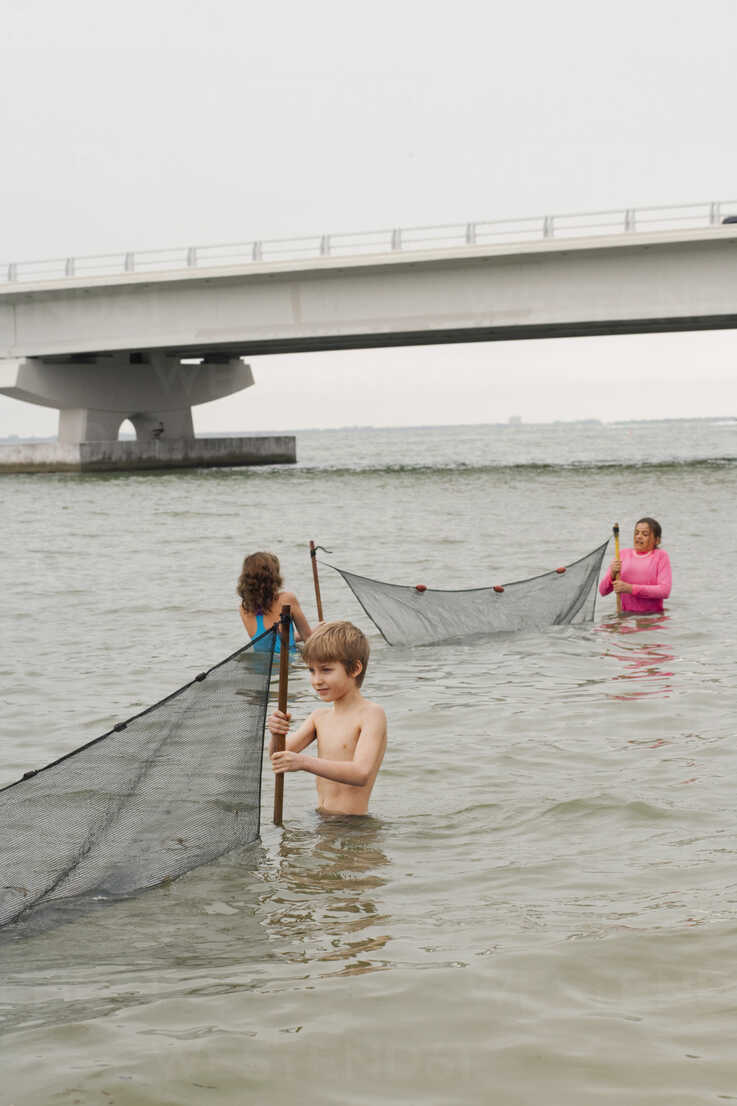 Children in ocean holding fishing nets and Sanibel causeway bridge, Sanibel  Island, Pine Island Sound, Florida, USA stock photo
