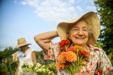 Senior woman holding onto straw hat and flowers on farm - ISF11504