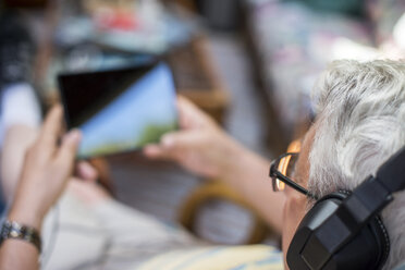 Senior man, sitting at home, wearing headphones, using digital tablet, elevated view - ISF11510