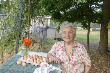 Senior woman posing beside tray of eggs on farm - ISF11511