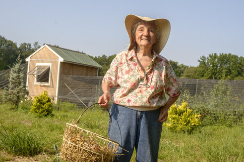 Ältere Frau trägt Korb mit Stroh auf dem Bauernhof - ISF11512