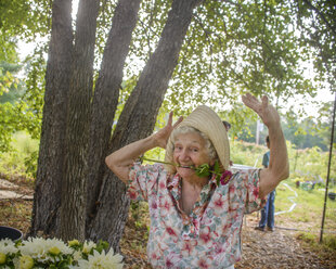 Ältere Frau mit Blume im Mund tanzt auf einem Bauernhof - ISF11514