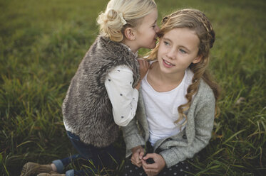 Young girl whispering in sister's ear, outdoors - ISF11547