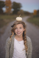 Young girl balancing small pumpkin on head - ISF11550