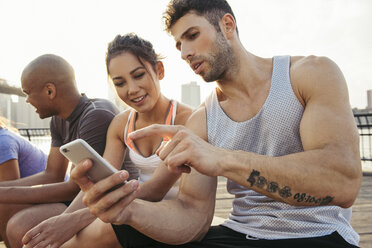 Young adult running friends using smartphone touchscreen on riverside, New York, USA - ISF11556