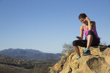 Läuferin wählt auf dem Gipfel eines Hügels die Musik ihres Smartphones, Thousand Oaks, Kalifornien, USA - ISF11599
