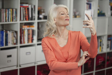 Mature woman taking self portrait, using smartphone, indoors - ISF11618