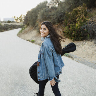 Junge Frau mit Gitarre, die lächelnd über die Schulter in die Kamera schaut, Woodland Hills, Kalifornien, USA - ISF11632