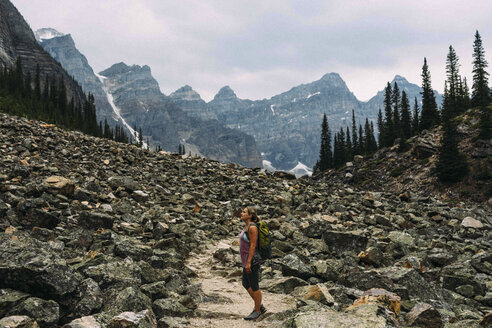 Seitenansicht einer mittelgroßen erwachsenen Frau in felsiger Landschaft unterhalb einer Bergkette, Moraine Lake, Banff National Park, Alberta Kanada - ISF11651