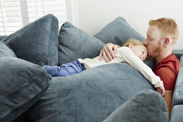 Father and daughter lying on pile of cushions in living room - ISF11656