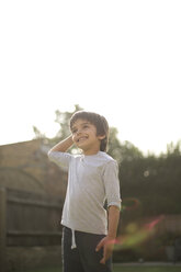 Niedriger Blickwinkel auf einen Jungen im Garten, der seine Hand auf den Kopf legt und lächelnd wegschaut - ISF11685