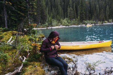 Mittlerer Erwachsener, am Kanu auf dem Moraine-See sitzend, nach unten blickend, wasserdichten Mantel befestigend, Banff National Park, Alberta Kanada - ISF11694