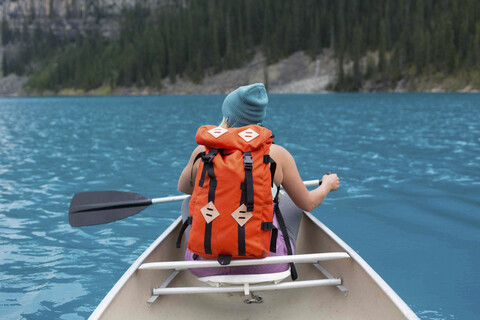 Rückansicht einer mittleren erwachsenen Frau mit orangefarbenem Rucksack beim Paddeln im Kanu, Moraine Lake, Banff National Park, Alberta Kanada, lizenzfreies Stockfoto