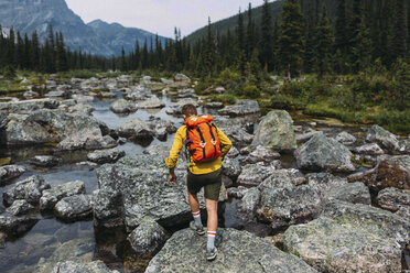 Rear view of mid adult man carrying backpack walking on rocky riverbed, Moraine lake, Banff National Park, Alberta Canada - ISF11696