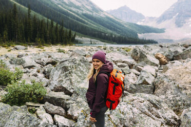 Seitenansicht einer mittelgroßen erwachsenen Frau auf einer Felslandschaft, die einen Rucksack trägt und lächelnd in die Kamera schaut, Moraine Lake, Banff National Park, Alberta Kanada - ISF11699