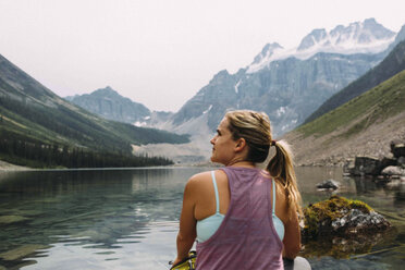 Rückansicht einer mittleren erwachsenen Frau, die am Ufer sitzt und wegschaut, Moraine Lake, Banff National Park, Alberta Kanada - ISF11700