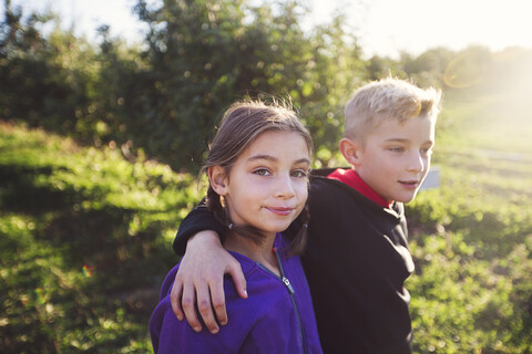 Boy in orchard with arms around girl, looking at camera smiling stock photo