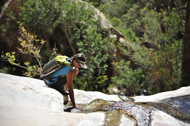 Young female rock climber crouching to touch water on rock, Mount Wilson, Nevada, USA - ISF11721