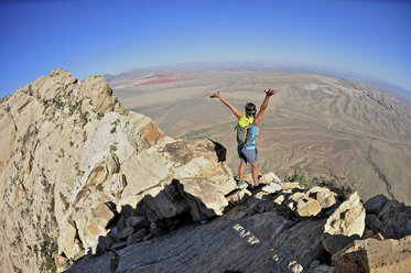 Rear view of young female rock climber with arms open on top of Mount Wilson, Nevada, USA - ISF11725