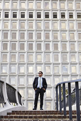 Business man standing at the top of stairway, wearing sunglasses, hands in pockets, looking away - ISF11732