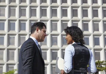 Business people standing talking face to face, holding paperwork, waist up - ISF11733