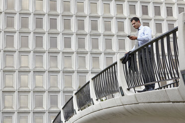 Mid adult business man standing on elevated walkway looking at smartphone - ISF11738