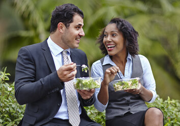 Business people sitting side by side enjoying a salad on lunch break, face to face, smiling - ISF11743