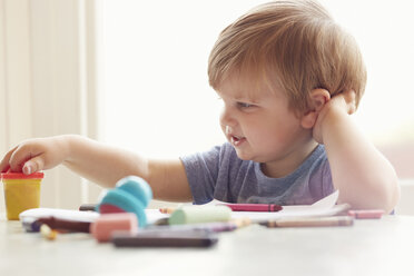 Boy sitting at table leaning on elbow looking at art supplies - ISF11749