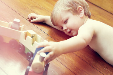 Hoher Blickwinkel auf einen Jungen, der auf dem Holzboden liegt und mit einer Spielzeugeisenbahn spielt - ISF11752