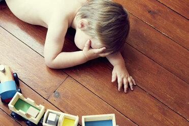 High angle view of boy lying on wooden floor by toy train, head in hand - ISF11753