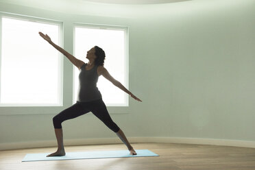 Mature woman doing yoga warrior pose in curved room - ISF11785