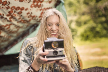 Porträt einer jungen Frau, die beim Camping mit einer Sofortbildkamera fotografiert - ISF11811