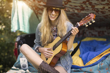 Porträt einer jungen Frau, die Ukulele spielt, während sie in einem Pick-up-Kofferraum zeltet - ISF11816