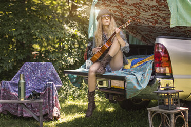 Junge Frau spielt Ukulele beim Camping im Pick-up-Kofferraum - ISF11818