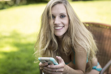 Porträt einer jungen Frau im Bikini mit Smartphone im Garten - ISF11829