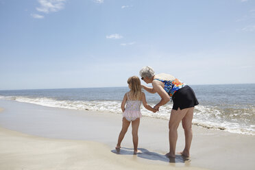 Ältere Frau, die am Strand auf ihre Enkelin zeigt - ISF11843