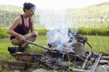 Female hiker making a campfire on lakeside, New Milford, Pennsylvania, USA - ISF11845