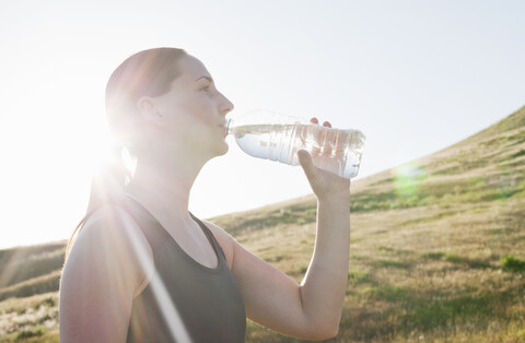 Junge Läuferin trinkt Wasser in Flaschen auf einem sonnenbeschienenen Berghang, lizenzfreies Stockfoto