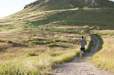 Rear view of young male runner running up hillside track - ISF11861