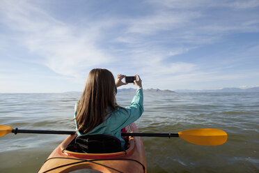 Rear view of young woman in kayak taking photograph, Great Salt Lake, Utah, USA - ISF11876