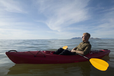 Side view of young man in kayak on water holding paddles, eyes closed, Great Salt Lake, Utah, USA - ISF11878