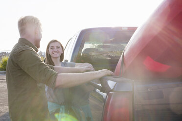 Junges Paar, das sich an einen Pick-up lehnt und sich lächelnd ansieht, Linsenreflexion - ISF11882