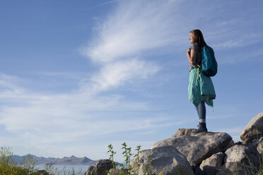 Rückansicht einer jungen Frau mit Rucksack, die auf einem Felsen steht und wegschaut, Great Salt Lake, Utah, USA - ISF11883