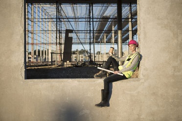 Architektin sitzt auf einem Fensterrahmen auf einer Baustelle - ISF11887