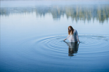 Young woman standing in middle of lake ripples looking down - ISF11906